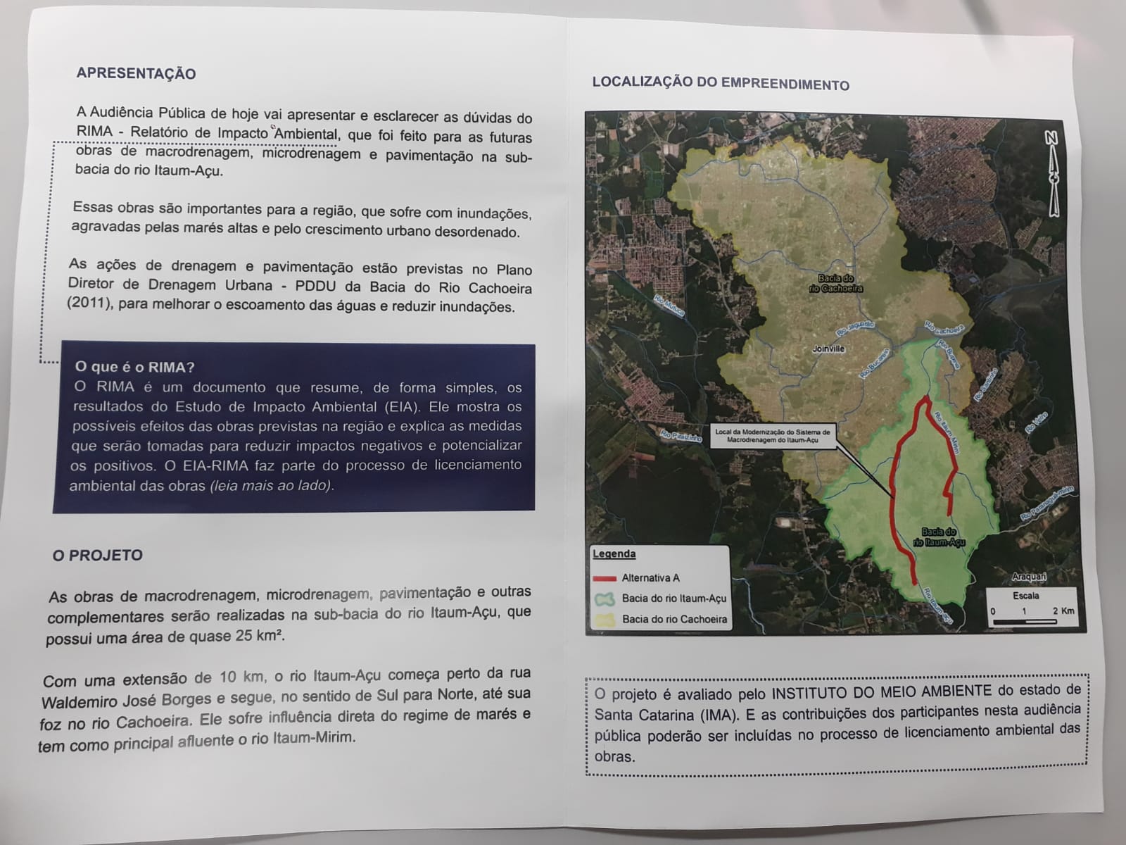 O panfleto comunica que a Audiência Pública tem como objetivo esclarecer dúvidas sobre o RIMA – Relatório de Impacto Ambiental, documento técnico elaborado para as obras de macrodrenagem, microdrenagem e pavimentação que ocorrerão na sub-bacia do rio Itaum-Açu, localizada no município de Joinville-SC.