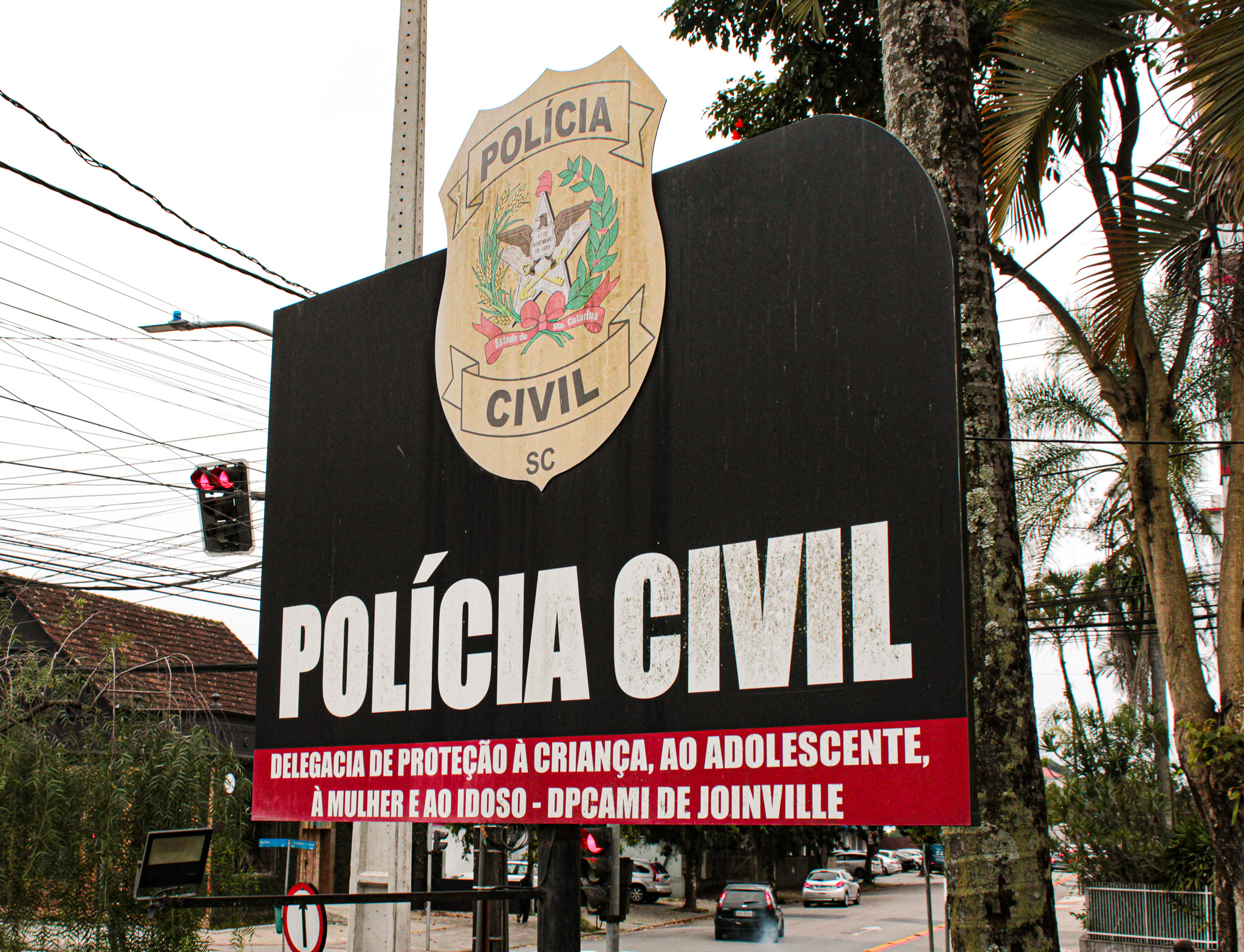 Placa de identificação da Polícia Civil de Santa Catarina em Joinville com fundo preto e faixa vermelha indicando a DPCAMI.