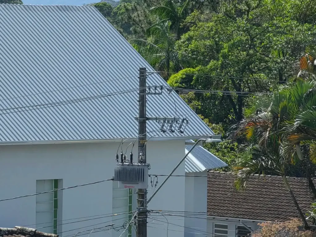 Poste de luz com diversos fios em uma rua arborizada.