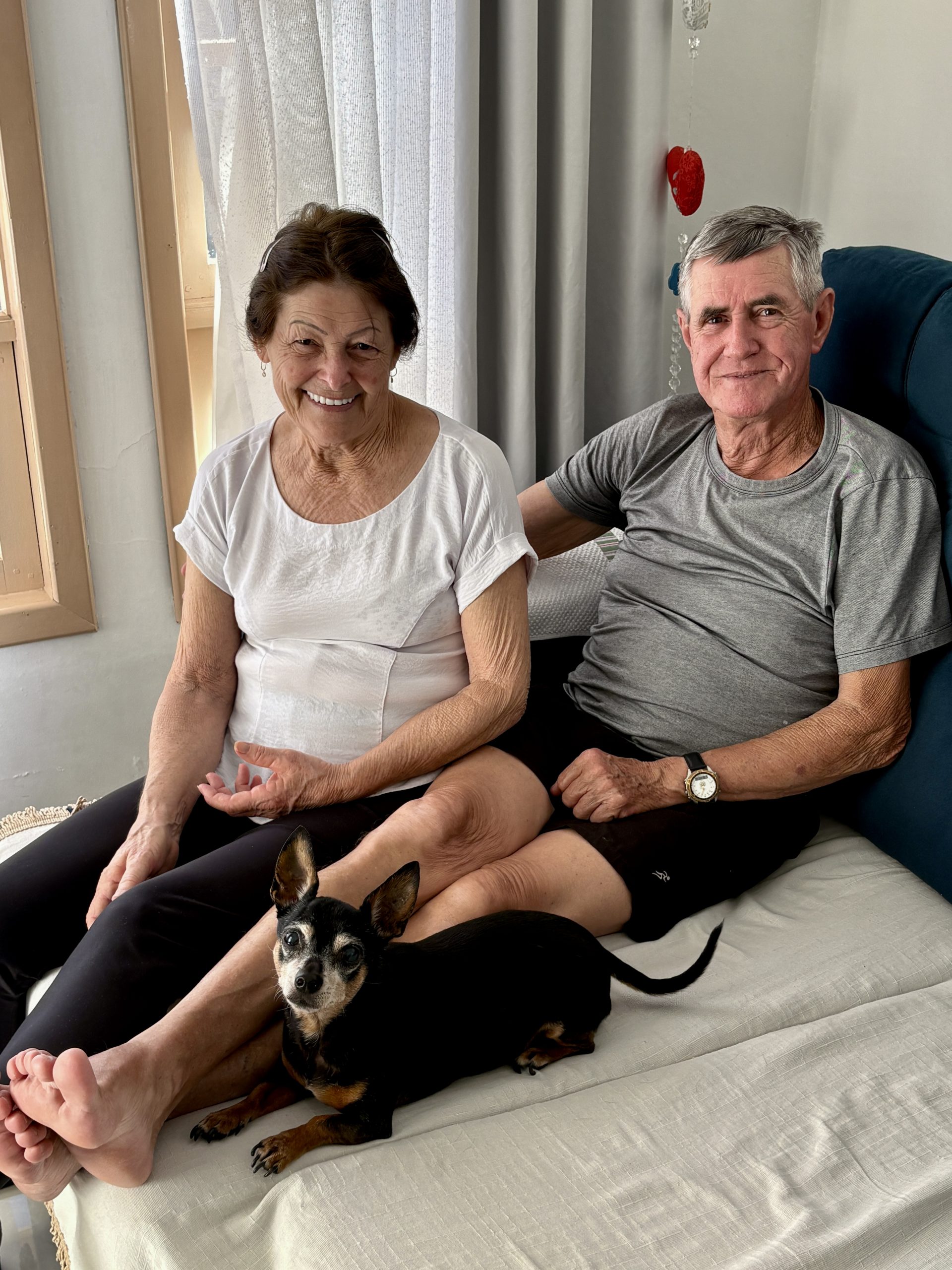 Mulher e homens idosos sentados em sofa azul. Junto deles tem um cachorrinho preto.