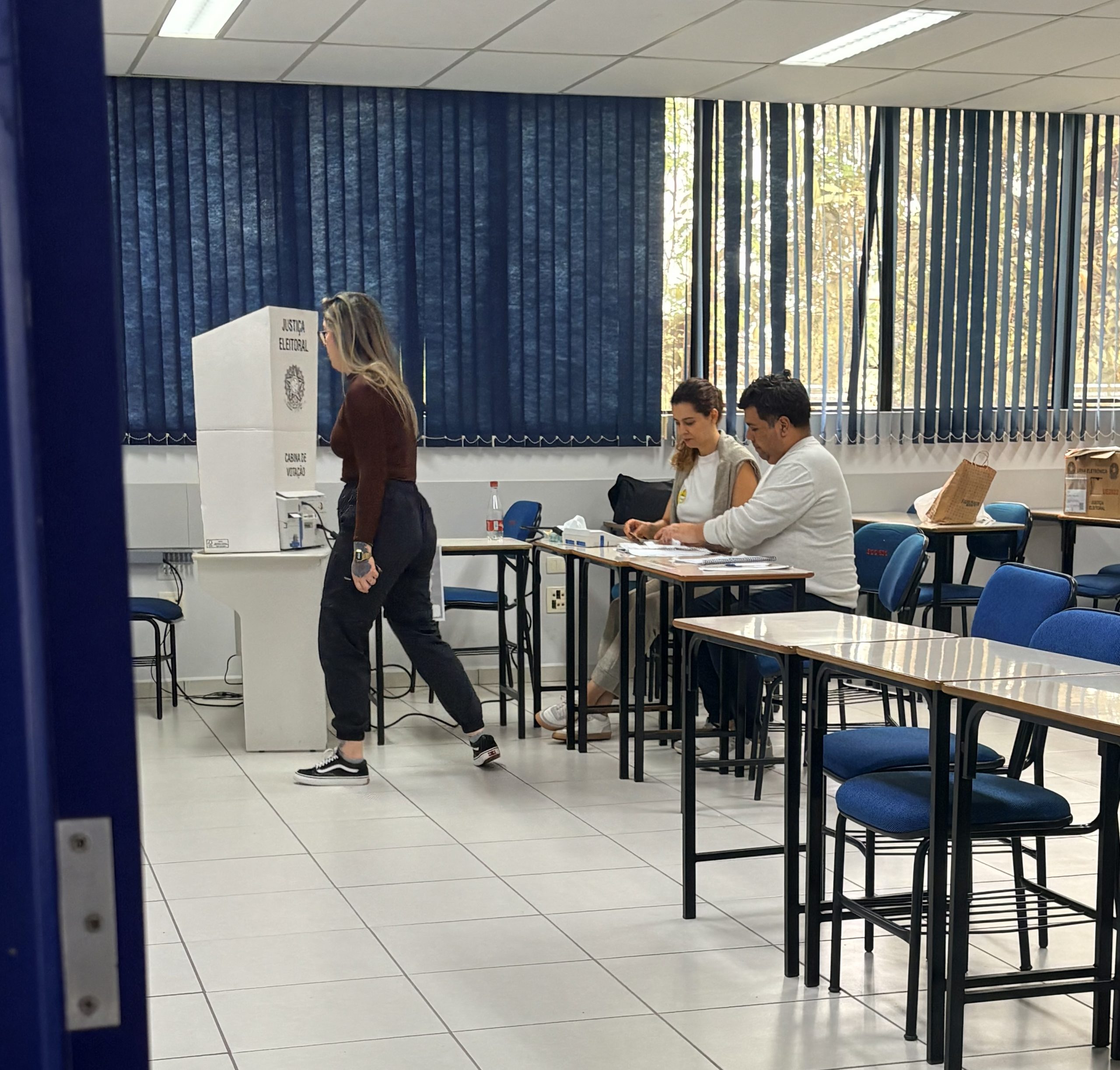 Eleitora em direção a urna, mesários acompanham