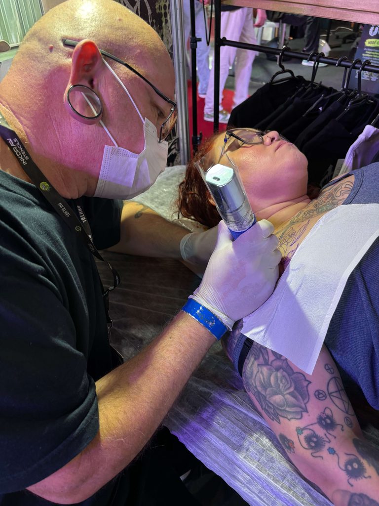 Renato Lima fazendo uma tatuagem no ombro de Michele Rodrigues.